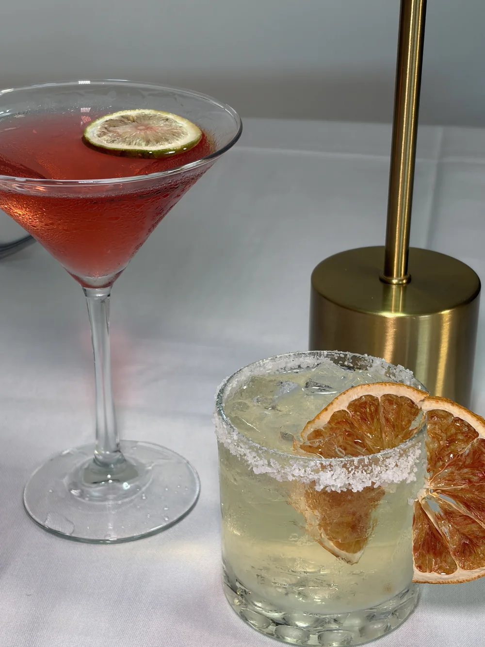 Two citrus-garnished cocktails beside a brass table lamp at Olive and Oak