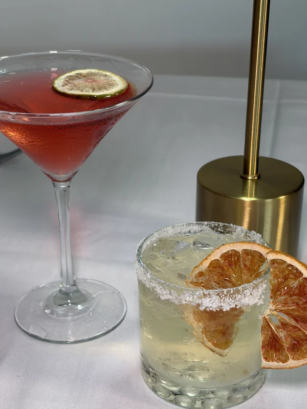 Two citrus-garnished cocktails beside a brass table lamp at Olive & Oak