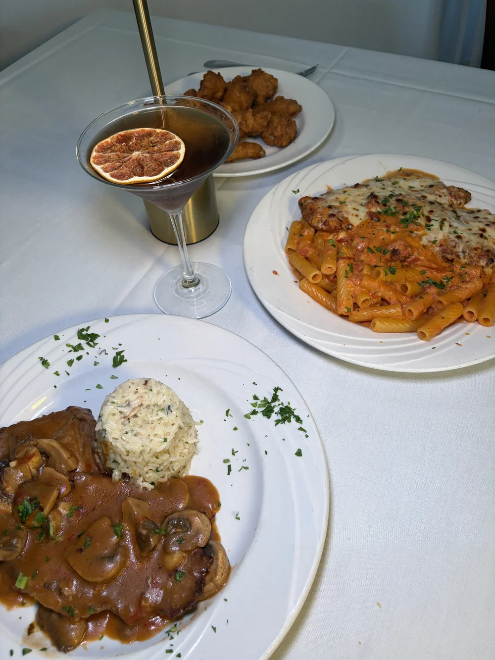 A dinner table at Olive and Oak with pasta, a mushroom-sauce entrée, rice, and a cocktail