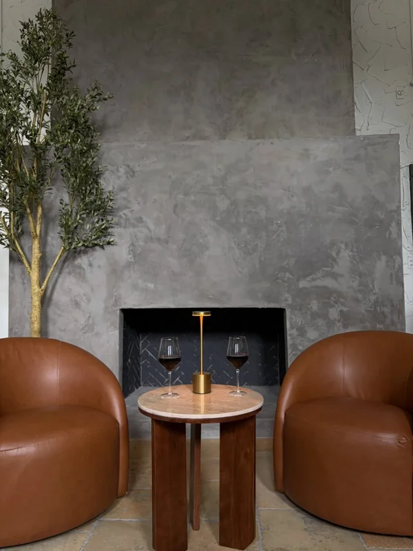 Two cognac leather chairs and glasses of red wine beside an olive tree and fireplace in the Olive & Oak lounge