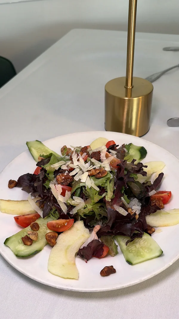 Mixed greens, shaved cheese, cucumber, tomatoes and nuts on a white plate at Olive & Oak