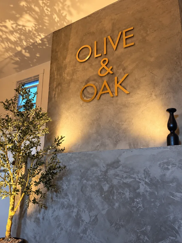Gold Olive & Oak lettering on a warmly lit plaster wall beside an olive tree