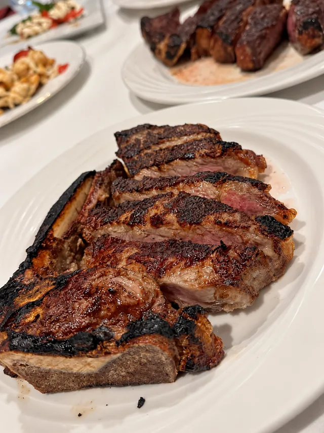 Grilled bone-in steak on a white platter at Olive & Oak